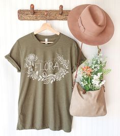 St. Flora, pray for us! This is a very comfortable, lightweight tee. Perfect for running errands, chasing toddlers, or picking flowers : ). Comes in two lovely colors: Heather Olive or Heather Magenta. 52% Airlume combed and ring-spun cotton, 48% poly, 32 single 4.2 oz. Care: Machine Wash Cold, inside out, on gentle cycle with a mild detergent. Please note that there may be slight variations in color due to photo lighting, differences in screen brightness, etc. *This product is shipped by our trusted printing partner (we do not ship these from our home). May be shipped separately if you order multiple items from our shop. Please let us know if you have any questions. Thanks for being here! : ) St. Flora is the special patroness of abandoned, converts, single laywomen, and victims of betray Spring T-shirt With Name Print In Relaxed Fit, Spring Relaxed Fit T-shirt With Name Print, Catholic Tshirts, Floral Tshirt, Picking Flowers, Pray For Us, Photo Lighting, Lovely Colors, Running Errands