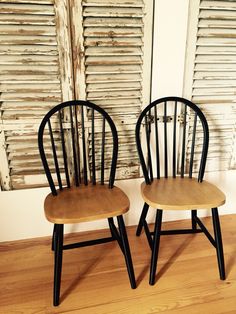 two wooden chairs sitting next to each other on top of a hard wood floor in front of shuttered windows