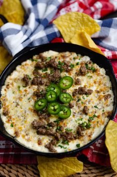 a black bowl filled with cheese and green peppers on top of tortilla chips