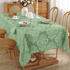 a dining room table covered with a green damask tablecloth and place settings for two