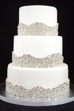 a three tiered white wedding cake with beading on the top and bottom layer