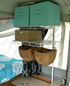 the inside of a camper with two baskets hanging from it's ceiling and a bed in the background