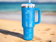 a blue travel mug sitting on top of a sandy beach