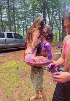 three girls covered in purple and pink paint are hugging each other while one girl is on her cell phone