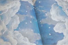 an open book with clouds and stars on it