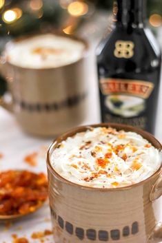 there is a cup of coffee with whipped cream in it next to two bottles of booze