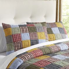 a bed with a white headboard and colorful quilts on the comforter in front of a window