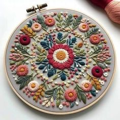 an embroidery project with flowers and leaves on the hoop, next to a yarn ball