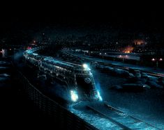 a train traveling down tracks next to a snow covered field at night with lights on