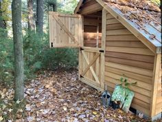 an outhouse in the woods with leaves on the ground and one door open to it