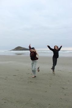 two women are running on the beach with their arms in the air and one is holding her hands up