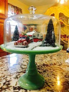 a green cake plate topped with a glass dome filled with snow covered trees and trains