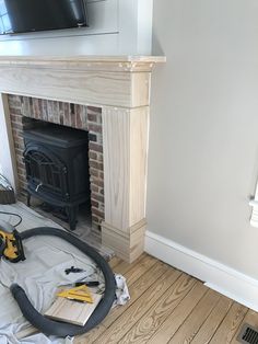 a room with a fire place and a tv on the wall, in front of a fireplace that is being worked on