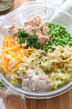 a glass bowl filled with pasta, peas and chicken salad on top of a wooden table