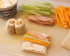 sandwiches with cheese, meat and vegetables on a cutting board next to a can of dip