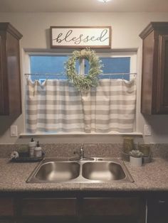 a kitchen sink under a window with a wreath on the valance and a sign above it