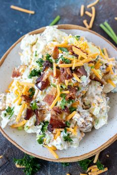 a white plate topped with potato salad covered in cheese and bacon next to green onions