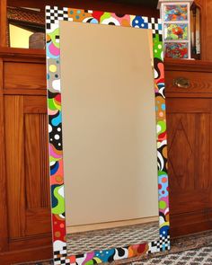 a colorful mirror sitting on top of a floor next to a wooden cabinet and door