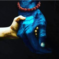 two hands painted in blue and gold holding each other's hand with beads around their wrists