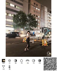 a woman standing in the middle of a street at night with buildings and cars behind her