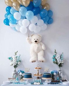 a white teddy bear sitting on top of a table next to blue and gold balloons