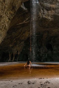 a woman is sitting in the water under a waterfall with her feet up on the ground