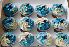 twelve cupcakes with blue and white frosting in a box on a table