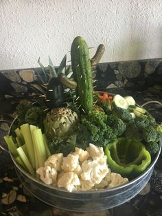 a bowl filled with lots of different types of vegetables on top of a marble counter