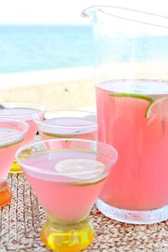 four glasses filled with watermelon and limeade sit on a table next to the ocean