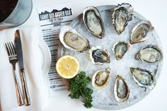 oysters on an ice tray with lemon wedges and silverware next to it