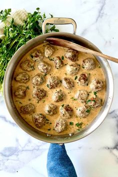 a pot filled with meatballs covered in gravy and garnished with parsley