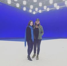 two women standing next to each other in front of a blue wall with lights on it