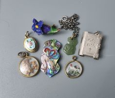 A nice lot to add to miniatures and antique jewellery collections. Reverse carved hand painted tiny crystal pendant. Glass encased tiny leaves double sided pendant. Cracked on one side. Jade nephrite kontiki miniature charm on a silver rolo link bracelet. Carved abalone kontiki figurine. Sterling silver Bible opening charm. No booklet present. Hand painted porcelain brooch pin. Old. Floral design...Iris? Tiny gold plated locket with appliqued guilloche enamel plaque. Antique Enamel Locket Jewelry, Antique Enamel Locket Necklace, Elegant Miniature Jewelry For Collectors, Antique Enamel Charms Jewelry, Antique Enamel Necklace Hallmarked, Antique Enamel Hallmarked Necklaces, Antique Enamel Necklace With Hallmark, Vintage Enamel Round Pendant Jewelry, Vintage Charm Round Enamel Jewelry