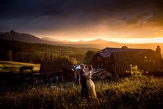 a bride and groom are standing in the grass at sunset with mountains in the background