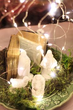 an open book sitting on top of a plate covered in moss and white figurines