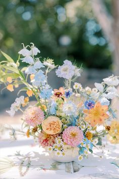 a vase filled with lots of colorful flowers on top of a white table covered in greenery