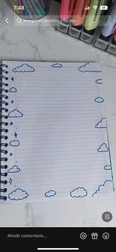 an open notebook with clouds and stars drawn on it next to some crayons