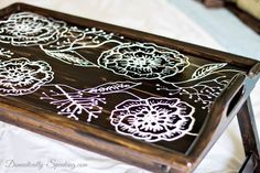 a wooden tray with white flowers painted on the top and bottom, sitting on a bed