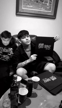 two young men sitting on a couch in front of a table with cups and drinks