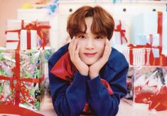 a young boy sitting in front of presents with his hands on his face and looking at the camera