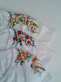 three white t - shirts with colorful flowers on them are laying next to each other