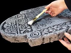 a person is holding a paintbrush and painting on a piece of stone with intricate designs