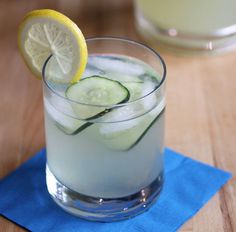 a drink with cucumber and lemon on the side sitting on a blue napkin