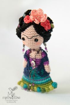 a small crocheted doll is wearing a dress and holding a flower in her hair