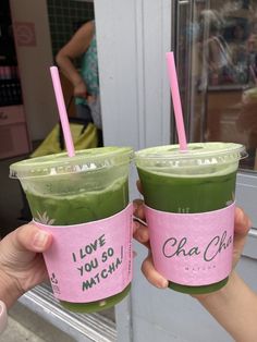 two people holding up cups with green smoothies in them