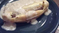 a blue plate topped with a hot dog covered in gravy on top of a wooden table