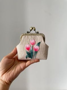 a hand holding a small purse with pink flowers on the front and green leaves on the back