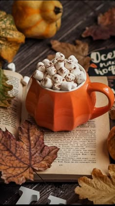 an orange mug filled with marshmallows sitting on top of an open book