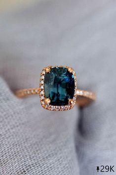 a ring with a blue stone surrounded by white and brown diamonds on top of a gray cloth