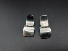 These sterling silver earrings were handmade in Mexico. They are made up of two rounded rectangles overlapping each other in heavy gauge silver. The smaller rectangle has the stud post and the larger hangs below and slightly behind it, dangling freely from a loop on the smaller piece. They have a great minimalist/modern design that would work for every day or a more formal occasion. They are in very good vintage condition but do have some light surface wear. Any yellow tones in the photos are th Minimalist Silver Drop Clip-on Earrings, Minimalist Oblong Earrings For Formal Occasions, Formal Minimalist Oblong Earrings, Modern Sterling Silver Oblong Earrings, Modern Oblong Sterling Silver Earrings, Silver Rectangular Earrings For Formal Occasions, Modern Silver Earrings With Rectangular Pendant, Modern Silver Rectangular Earrings, Minimalist Silver Clip-on Earrings For Everyday